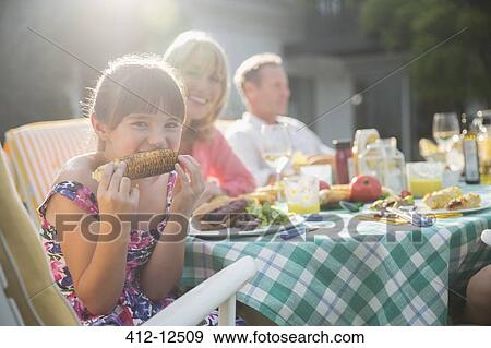 Girl eating corncob at table in backyard View Large Photo Image Stock Photo - Girl eating corncob at table in backyard. Fotosearch