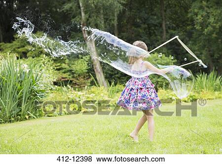 Girl making large bubbles in backyard View Large Photo Image Stock Photo - Girl making large bubbles in backyard. Fotosearch