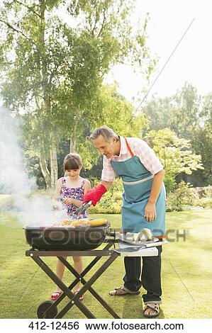 Stock Photograph - Grandfather and granddaughter grilling at barbecue in backyard. Fotosearch