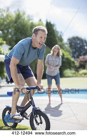 Picture - Man riding small bicycle at poolside. Fotosearch
