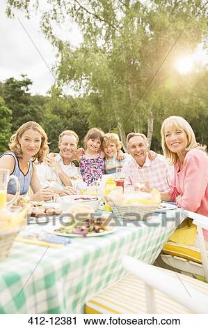 Stock Image - Multi-generation family eating lunch at table in backyard. Fotosearch