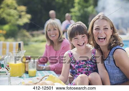 Stock Image - Multi-generation family laughing at table in backyard. Fotosearch