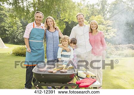 Stock Image - Multi-generation family standing at barbecue in backyard. Fotosearch