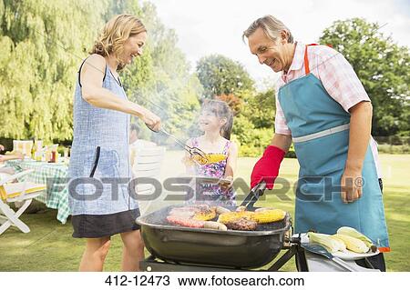 Stock Image - Multi-generation family standing at barbecue in backyard. Fotosearch