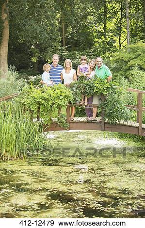 Stock Photo - Multi-generation family standing on wooden footbridge over pond. Fotosearch