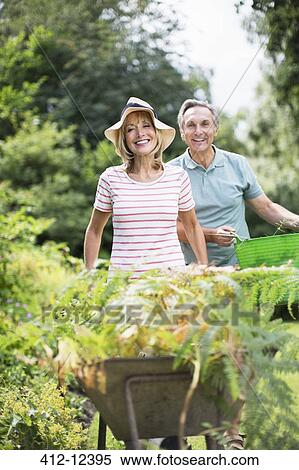 Stock Photography - Senior couple with wheelbarrow and bucket in garden. Fotosearch