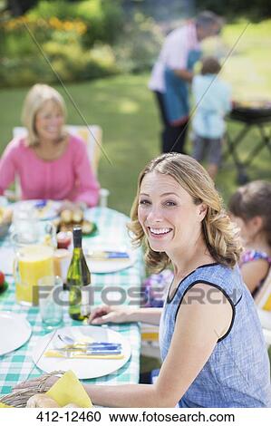 Stock Image - Woman smiling at table in backyard. Fotosearch