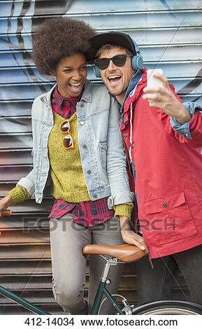 Picture - Couple taking self-portrait with cell phone against graffiti wall. Fotosearch