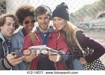 Stock Image - Friends taking self-portrait with camera phone outdoors. Fotosearch