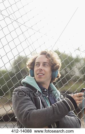 Man listening to headphones against chain link fence View Large Photo Image Stock Photo - Man listening to headphones against chain link fence. Fotosearch