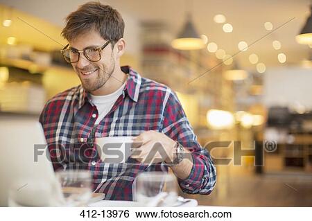 Stock Photograph - Man using laptop and drinking coffee in cafe. Fotosearch