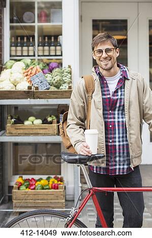 Stock Photo - Man with coffee cup and bicycle on city street. Fotosearch