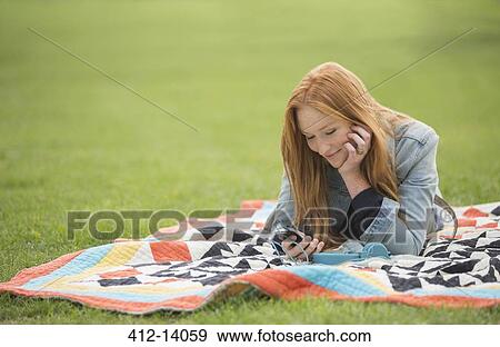 Woman using cell phone on blanket in park View Large Photo Image Stock Photo - Woman using cell phone on blanket in park. Fotosearch