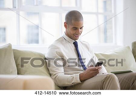 Stock Image - Businessman using cell phone on sofa. Fotosearch