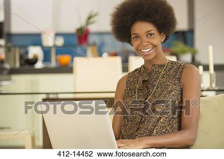 Stock Image - Businesswoman using laptop in kitchen. Fotosearch