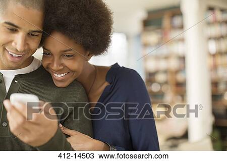 Stock Image - Couple using cell phone in living room. Fotosearch