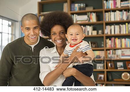 Stock Image - Family smiling together in living room. Fotosearch