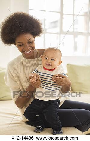 Stock Photograph - Mother and baby boy playing on sofa. Fotosearch