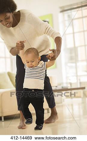 Mother helping baby boy walk in living room View Large Photo Image Stock Photo - Mother helping baby boy walk in living room. Fotosearch