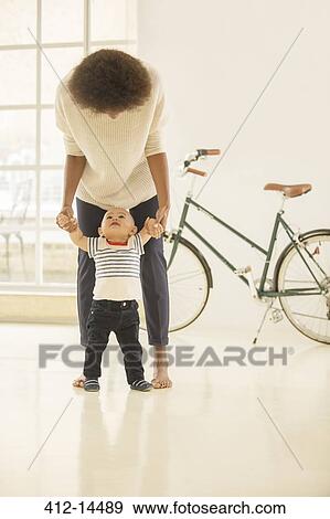 Mother helping baby boy walk in living room View Large Photo Image Stock Photo - Mother helping baby boy walk in living room. Fotosearch