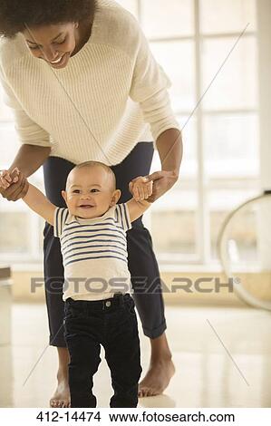 Mother helping baby boy walk on floor View Large Photo Image Picture - Mother helping baby boy walk on floor. Fotosearch
