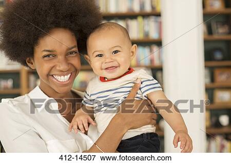 Stock Photo - Mother holding baby boy in living room. Fotosearch
