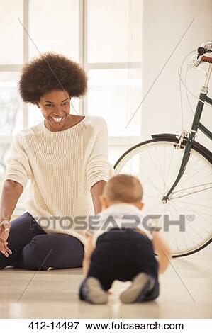 Stock Photo - Mother watching baby boy crawl in living room. Fotosearch