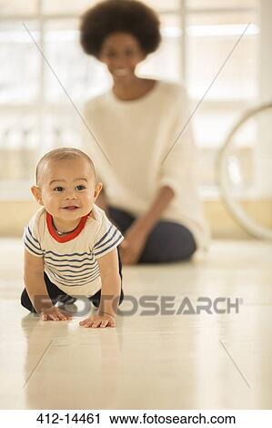 Stock Image - Mother watching baby boy crawl on floor. Fotosearch