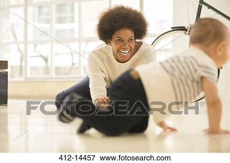 Mother watching baby boy crawl on living room floor View Large Photo Image Stock Photo - Mother watching baby boy crawl on living room floor. Fotosearch