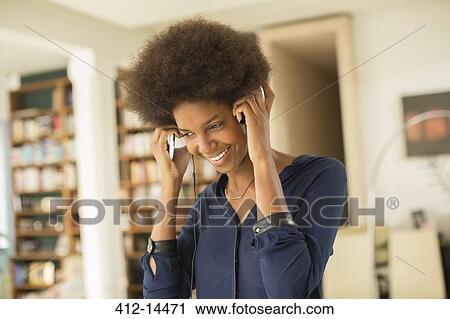 Stock Image - Woman listening to headphones in living room. Fotosearch