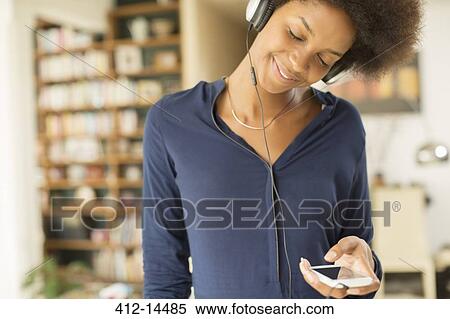 Woman listening to headphones in living room View Large Photo Image Stock Photography - Woman listening to headphones in living room. Fotosearch