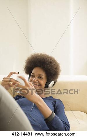 Stock Image - Woman listening to headphones on sofa. Fotosearch
