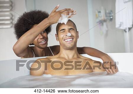 Stock Photograph - Woman playing with boyfriend in bubble bath. Fotosearch