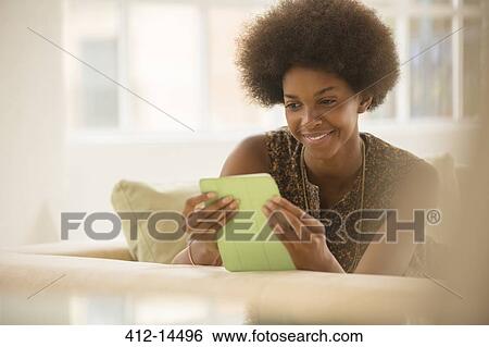 Stock Photograph - Woman using digital tablet on sofa. Fotosearch