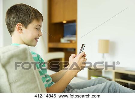 Boy using cell phone in living room View Large Photo Image Stock Photograph - Boy using cell phone in living room. Fotosearch