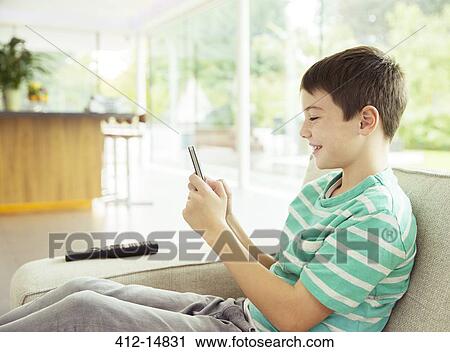 Stock Image - Boy using cell phone on sofa. Fotosearch