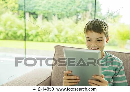 Boy using digital tablet in living room View Large Photo Image Stock Image - Boy using digital tablet in living room. Fotosearch