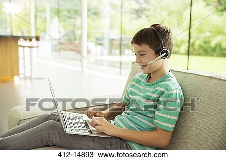 Boy wearing headset and using laptop on sofa View Large Photo Image Stock Image - Boy wearing headset and using laptop on sofa. Fotosearch