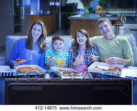 Stock Photography - Family eating pizza in front of television in living room. Fotosearch