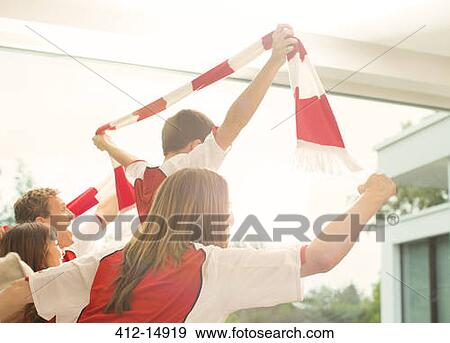 Family in sports jerseys cheering in living room View Large Photo Image Stock Photo - Family in sports jerseys cheering in living room. Fotosearch