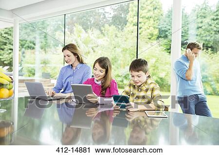 Family using technology in kitchen View Large Photo Image Stock Image - Family using technology in kitchen. Fotosearch
