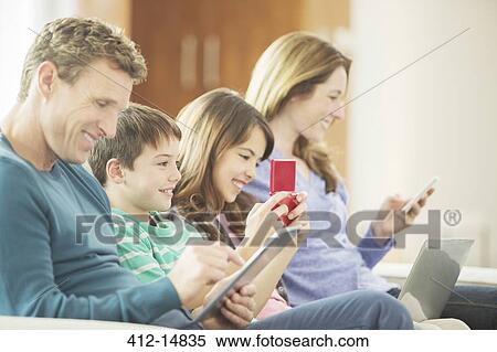 Stock Photography - Family using technology on sofa. Fotosearch