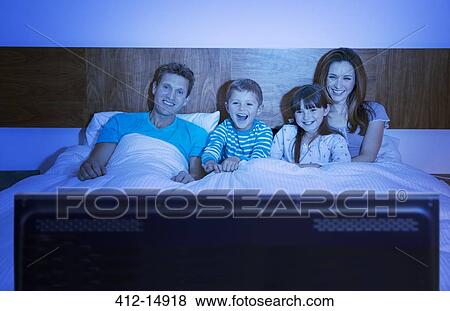Stock Photo - Family watching television in bed. Fotosearch