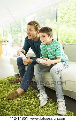 Father and son playing video games in living room View Large Photo Image Stock Image - Father and son playing video games in living room. Fotosearch