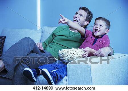Father and son watching television in living room View Large Photo Image Stock Photo - Father and son watching television in living room. Fotosearch