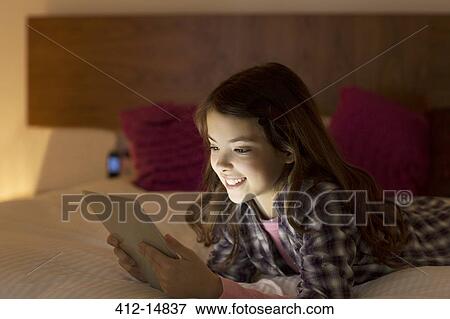 Stock Photo - Girl using digital tablet on bed. Fotosearch