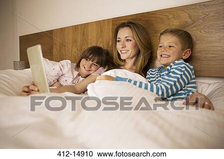 Mother and children using digital tablet in bed View Large Photo Image Stock Image - Mother and children using digital tablet in bed. Fotosearch
