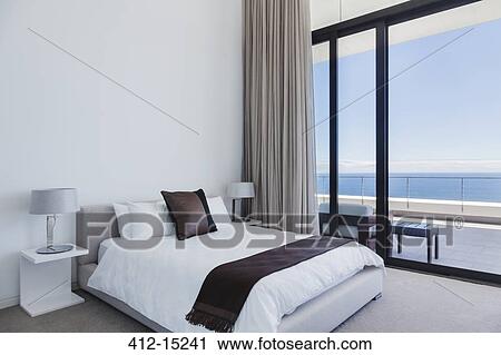 Stock Image - Bed and lamps in modern bedroom overlooking ocean. Fotosearch