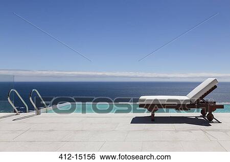 Stock Photograph - Infinity pool and lounge chair overlooking ocean. Fotosearch