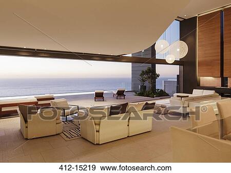 Stock Photo - Living room in modern house overlooking ocean at sunset. Fotosearch